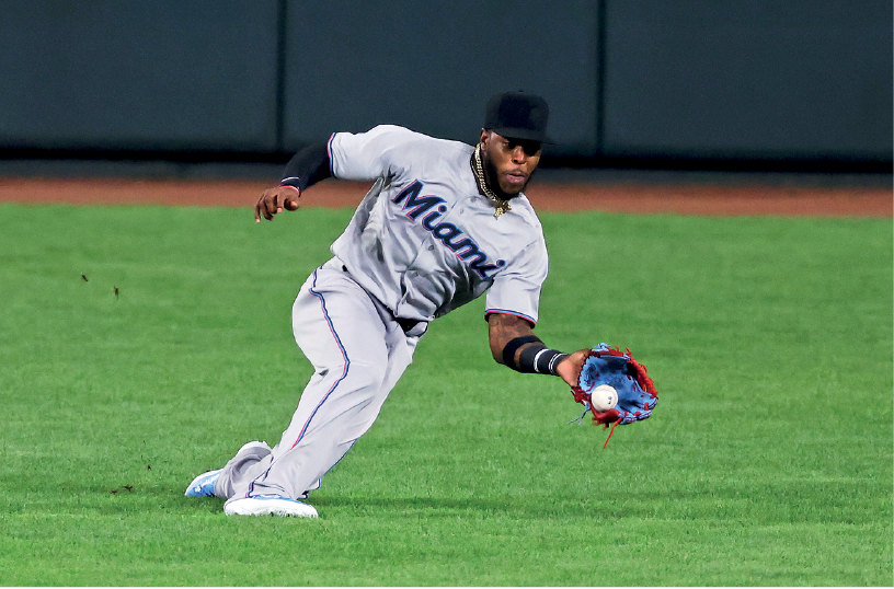 Imagem: Fotografia. Um homem com boné preto, uniforme branco, segurando uma luva com a mão esquerda, e uma bola de beisebol. Fim da imagem.