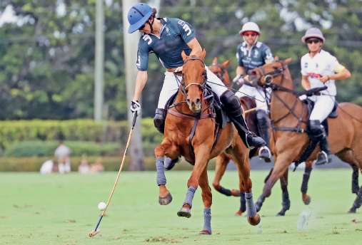 Imagem: Fotografia. Três pessoas uniformizadas, usando capacete, montados em cavalos segurando um bastão, próximo a uma bola no gramado. Fim da imagem.