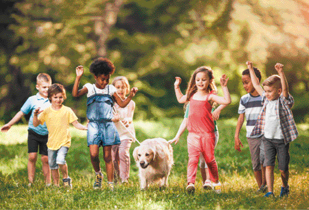 Imagem: Fotografia. Oito crianças correndo em um parque. Da esquerda para a direita: um menino loiro de bermuda preta e camiseta azul. Um menino de cabelo castanho liso usando uma bermuda jeans e camiseta amarela. Uma menina negra de cabelo curto usando um vestido jeans. Uma menina loira de cabelo curto usando uma blusa bege e calça rosa; ela segura a coleira de um cachorro bege. Uma menina de camiseta verde que está com a mão no cachorro. Uma menina de cabelo castanho liso com os braços erguidos, usando um macacão vermelho. Um menino moreno de camiseta azul listrada. Um menino loiro com os braços erguidos, camiseta verde, bermuda cinza e camisa xadrez por cima.  Fim da imagem.
