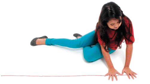 Imagem: Fotografia. Uma menina de cabelo castanho sentada no chão. Ela usa uma sapatilha, calça jeans e camiseta vermelha. A menina está com as duas mãos abertas lado a lado em cima de uma corda que está esticada ao seu lado.   Fim da imagem.