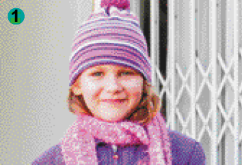 Imagem: Fotografia. Uma menina loira de cabelo ondulado usando um casaco roxo, um cachecol rosa e gorro de lã listrado.  Fim da imagem.
