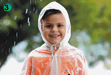 Imagem: Fotografia. Um menino de cabelo castanho usando uma camiseta laranja e uma capa de chuva transparente por cima.   Fim da imagem.