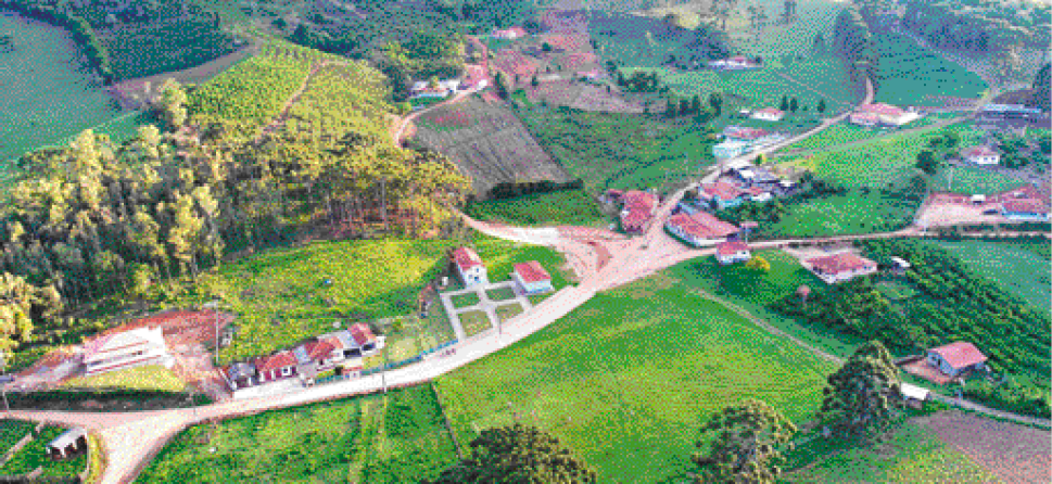 Imagem: Fotografia. Vista aérea de um campo gramado com algumas estradas de terra, áreas com árvores, plantações e algumas construções espaçadas.  Fim da imagem.