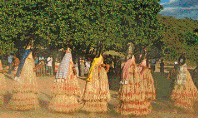 Imagem: Fotografia. Várias mulheres enfileiradas com roupas de palha.  Fim da imagem.