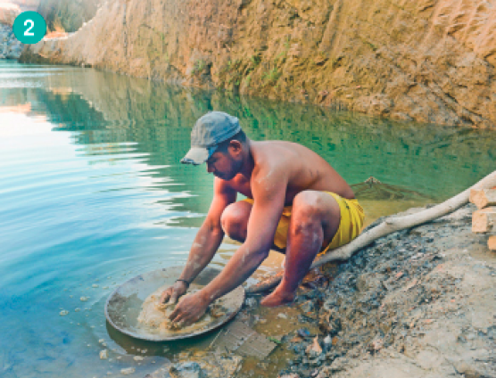 Imagem: Fotografia. Um homem sem camisa de bermuda amarela e boné. Ele está abaixado ao lado de um rio mexendo em uma cumbuca com terra.  Fim da imagem.