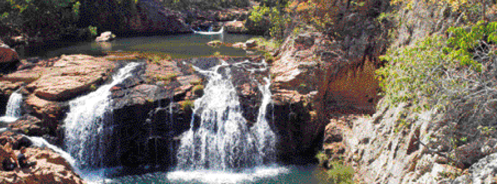 Imagem: Fotografia. Uma cachoeira baixa, com a água escorrendo entre pedras.  Fim da imagem.