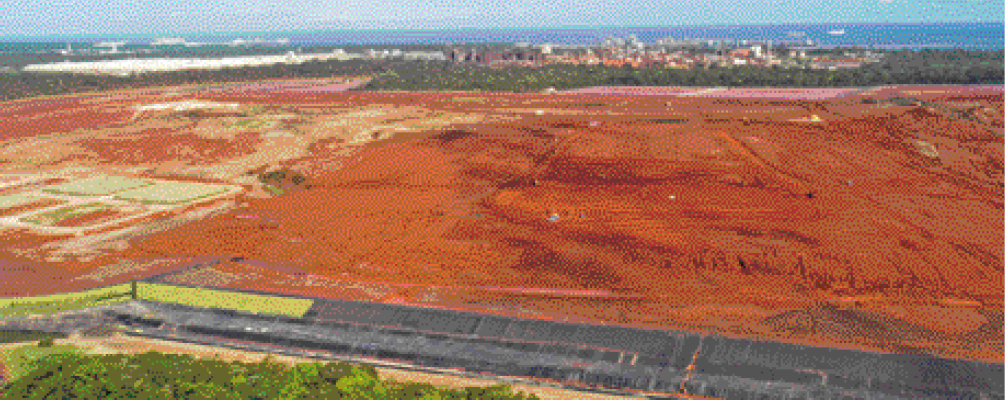 Imagem: Fotografia. Um grande campo de terra. No fundo, uma cidade.   Fim da imagem.