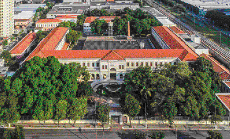 Imagem: Fotografia. Um palácio com dois andares e um jardim com árvores na frente.  Fim da imagem.