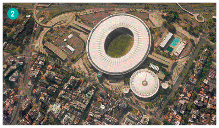 Imagem: Fotografia. Vista aérea de uma cidade, com um grande estádio de futebol no meio.  Fim da imagem.