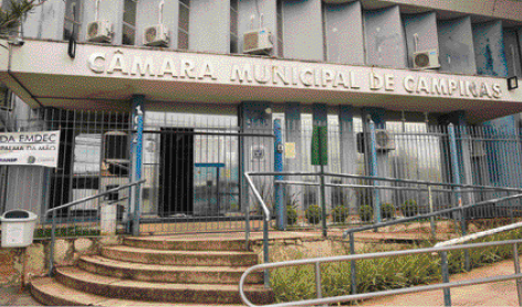 Imagem: Fotografia. Fachada da Câmara Municipal de Campinas. Prédio antigo e cinza, com uma grade azul na frente, escada e uma rampa.   Fim da imagem.