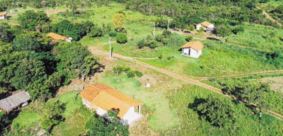 Imagem: Fotografia. Imagem aérea de cinco casas espaçadas, em uma zona rural. Ao redor das casas há áreas gramadas e árvores.  Fim da imagem.