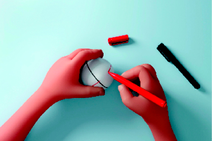 Imagem: Fotografia. Destaque para a mão de uma pessoa traçando uma linha vertical em uma bolinha de isopor com uma caneta vermelha. Na mesa há uma caneta preta.  Fim da imagem.