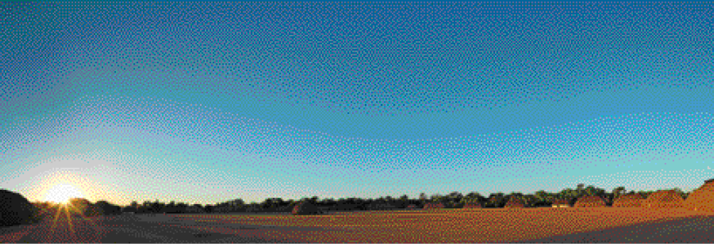 Imagem: Fotografia. Uma paisagem de um campo aberto com o sol no horizonte, do lado esquerdo.   Fim da imagem.