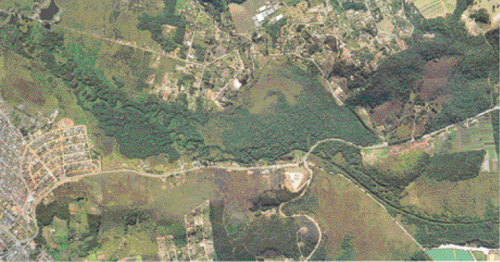 Imagem: Fotografia. Imagem aérea de uma área rural com partes cobertas de vegetação e áreas de construções. Fim da imagem.