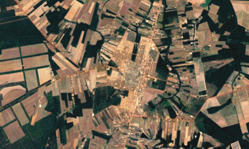 Imagem: Fotografia. Imagem aérea de uma região, com partes retangulares e um centro urbano no centro. Fim da imagem.
