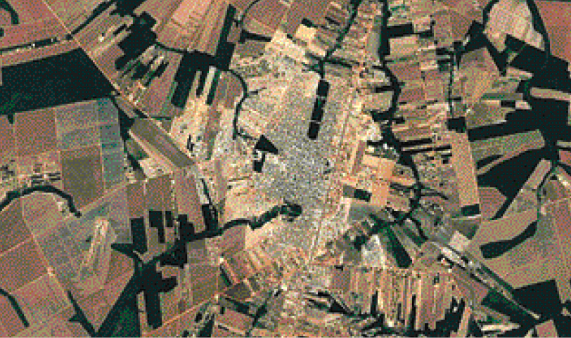 Imagem: Fotografia. Imagem aérea de uma região, com partes retangulares e um centro urbano grande. Fim da imagem.