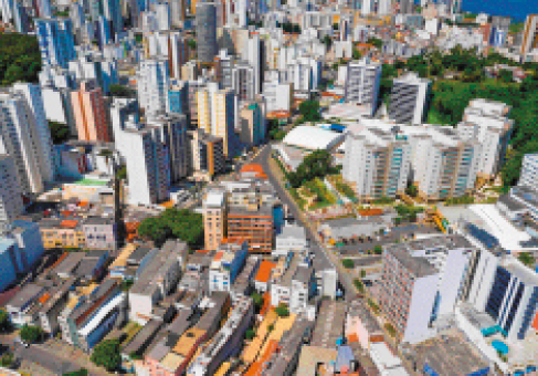 Imagem: Fotografia. Imagem aérea de uma cidade com prédios de diferentes alturas.  Fim da imagem.