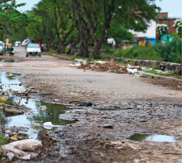 Imagem: Fotografia. Uma rua de terra com um carro no fundo. Há poças de água nas guias.  Fim da imagem.