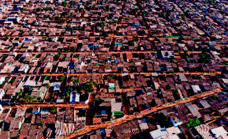 Imagem: Fotografia. Vista aérea de uma cidade com casas e ruas paralelas na horizontal. Fim da imagem.