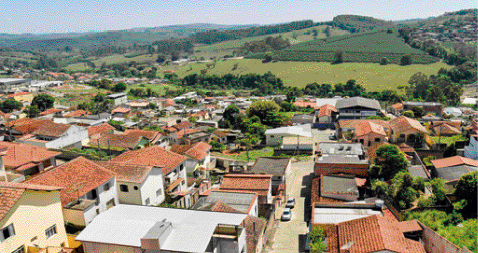 Imagem: Fotografia. Uma cidade vista de cima. No plano principal, casas e ruas. No fundo, área rural.  Fim da imagem.