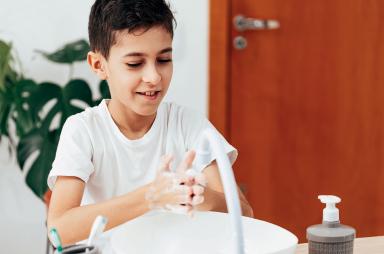 Imagem: 1. Fotografia. Um menino lava as mãos na pia. Fim da imagem.