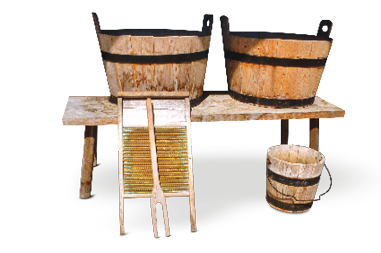 Imagem: Fotografia. Duas grandes tinas sobre uma bancada na qual está encostada uma tábua com relevos em madeira ao lado de um balde. Fim da imagem.