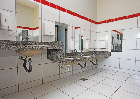 Imagem: Fotografia. Destaque do interior de um banheiro que apresenta um conjunto de pias em nível mais baixo e uma pia em nível mais alto. Há espelho nas paredes. Fim da imagem.