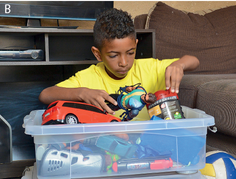 Imagem: Fotografia. Na sala, um menino ajeita os brinquedos em uma caixa.  Fim da imagem.