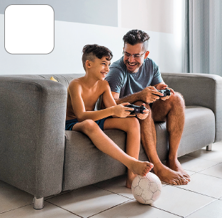 Imagem: Fotografia. Na sala, um homem e um garoto jogam videogame sentados no sofá lado a lado. O menino está sem camisa e com os pés sobre uma bola de futebol e o homem de camiseta, shorts e descalço. Ambos sorriem.  Fim da imagem.