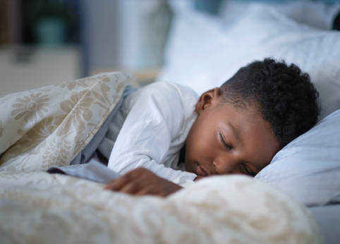 Fotografia 6. Um menino de pijama dorme deitado em sua cama.