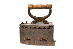 Imagem: Fotografia. Um ferro de passar antigo, composto por uma tampa fechada com rebarbas e uma alça de madeira.  Fim da imagem.
