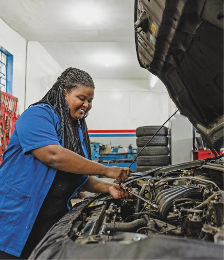 Imagem: Fotografia. Uma mulher de jaleco azul sorri enquanto manipula cabos do equipamento interno de um veículo.  Fim da imagem.