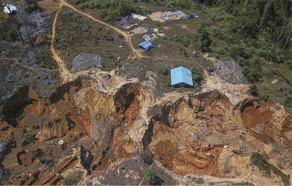 Imagem: Fotografia. Vista aérea de uma área com muitas rochas, pequenas construções e muitas árvores ao redor.  Fim da imagem.