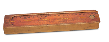 Imagem: Fotografia. Um estojo de madeira que apresenta a o fechamento da parte superior com uma régua deslizante. Fim da imagem.
