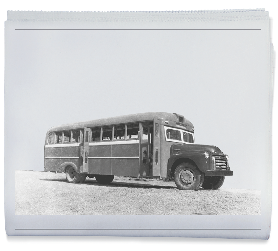Imagem: Fotografia em preto e branco. Um ônibus vazio com a frente comprida e vidros retangulares. Na lateral há duas portas abertas e janelas quadradas.  Fim da imagem.