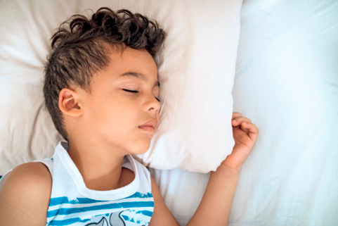 Imagem: Fotografia. Um menino dorme de lado deitado em seu travesseiro.  Fim da imagem.