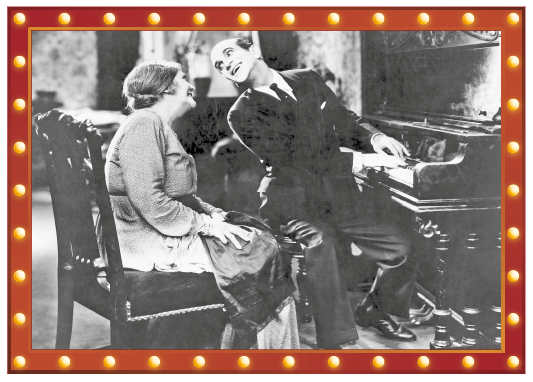 Imagem: Fotografia em preto e branco. Em uma sala, um homem de terno toca piano e sorri olhando para uma mulher sentada em uma cadeira atrás dele. Fim da imagem.