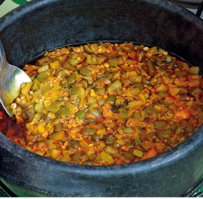 Imagem: Fotografia. Uma panela de ferro com alimento ensopado com quiabo. Fim da imagem.