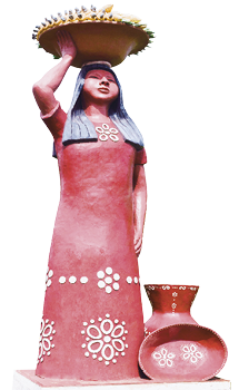 Imagem: Fotografia. Uma escultura de uma mulher de longo vestido de pé equilibrando um cesto cheio na cabeça. Ao lado, um vaso e uma travessa com a mesma estampa de seu vestido. Fim da imagem.