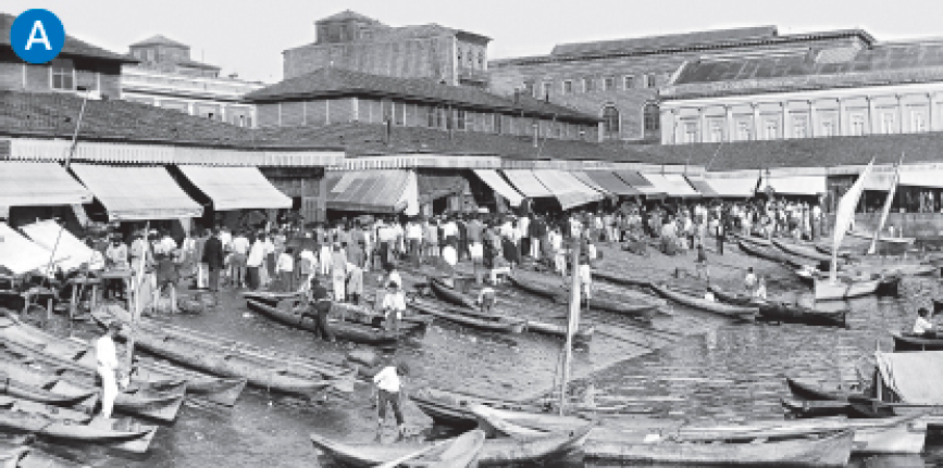 Imagem: A. Fotografia em preto e branco. Destaque de uma faixa à beira-mar com pequenas embarcações e muitas barracas com toldos ao redor. Ao fundo, grandes construções.  Fim da imagem.