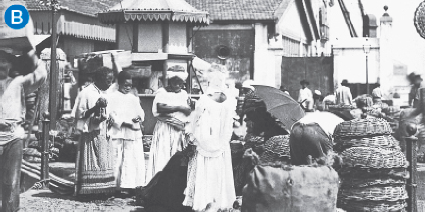 Imagem: B. Fotografia em preto e branco. Ao centro, mulheres de pé próximas de cestos. Ao redor, há construções simples e homens trabalhando. Fim da imagem.