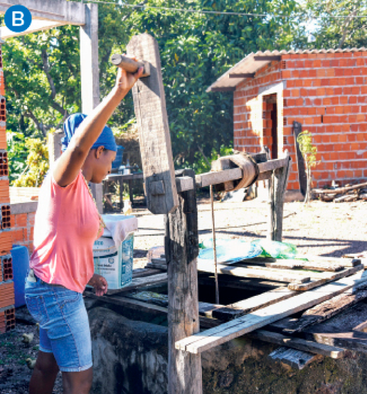 Imagem: Fotografia. Uma mulher de camisa, shorts e tecido na cabeça manipula a manivela de um poço com estrutura de madeira enquanto olha para a corda.  Fim da imagem.