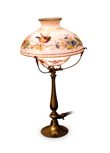 Imagem: Fotografia. Um lampião com base de aspecto bronzeado estreito e alto e cúpula com formato semicircular branco com desenho de flores e um pássaro.  Fim da imagem.