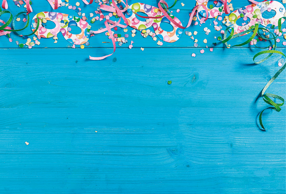 Imagem: Fotografia. Uma composição com máscaras carnavalescas, confetes e serpentinas coloridas sobre uma superfície de madeira pintada de azul. Fim da imagem.