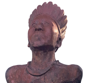 Imagem: Fotografia. Busto de uma escultura de um homem indígena que usa um cocar, adereço no pescoço e olha para cima. Fim da imagem.