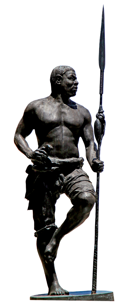 Imagem: Fotografia. Uma escultura de homem negro de pé que usa uma calça curta e está sem camisa. Ele segura uma lança comprida apoiada no chão, segura um objeto na cintura e está com o pé esquerdo apoiado no joelho direito. Fim da imagem.