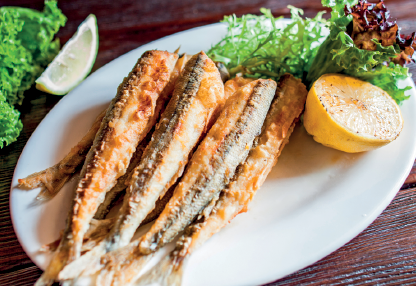Imagem: Fotografia. Um prato que apresenta peixes fritos lado a lado com rodelas de limão cortadas e folhas. Fim da imagem.
