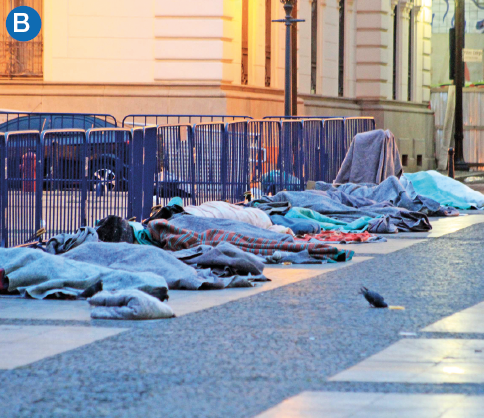 Imagem: B. Fotografia. Destaque de uma ampla calçada onde dormem muitas pessoas cobertas lado a lado. Fim da imagem.