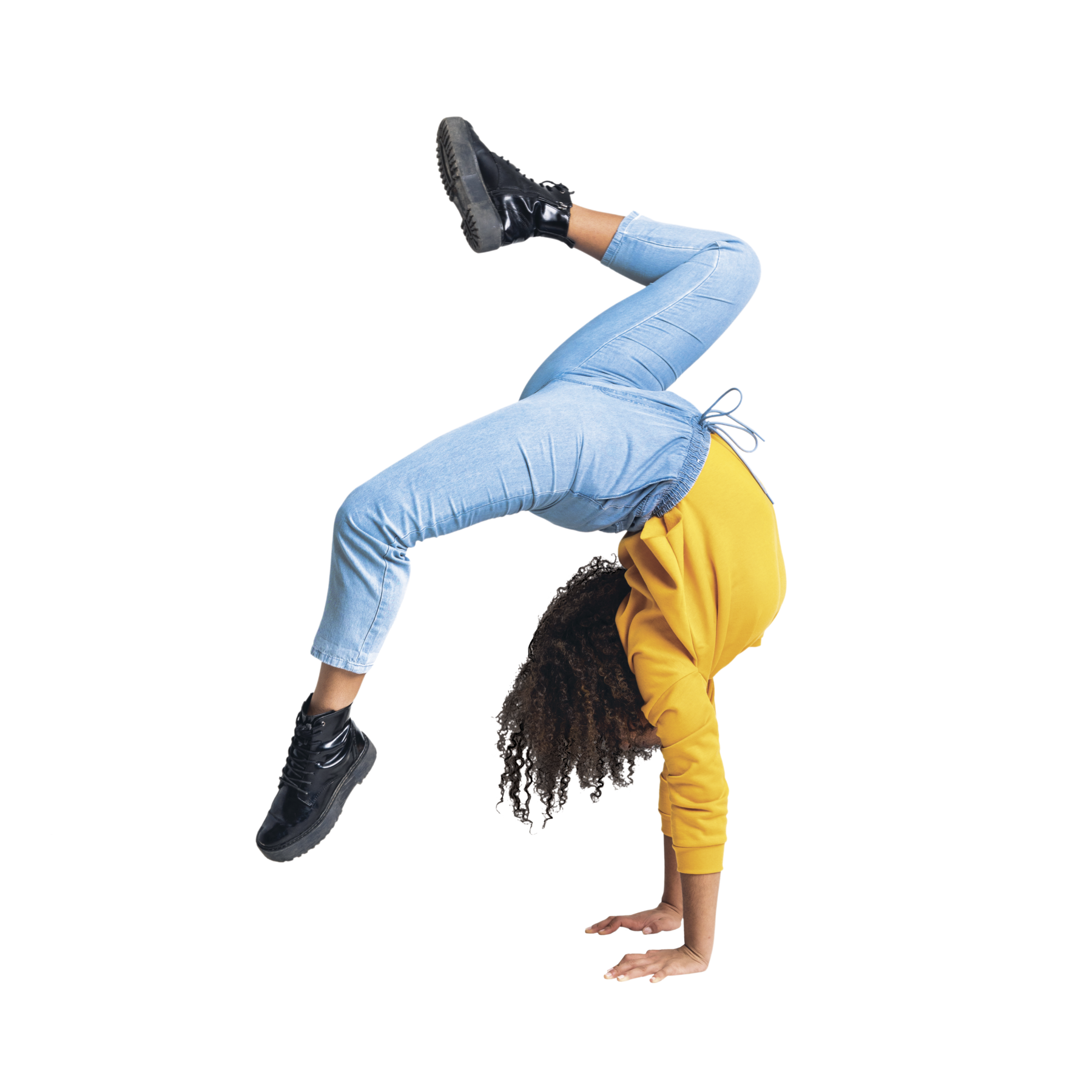 Fotografia. Moça com cabelos castanhos cacheados compridos, blusa amarela, calça azul e tênis preto. Ela está com as duas mãos apoiadas no chão e com as pernas no ar, flexionadas.