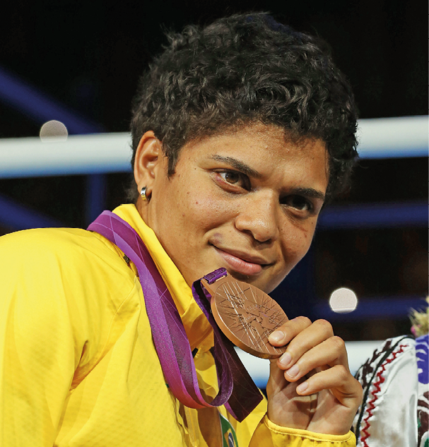 Fotografia. Adriana Araújo sorrindo e segurando uma medalha de bronze no peito.